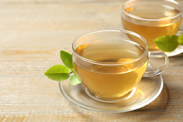 Cups of green tea and leaves on wooden table