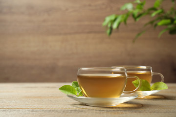 Cups of green tea and leaves on wooden table. Space for text