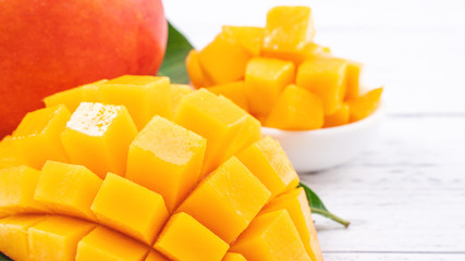 Fresh mango,beautiful chopped fruit with green leaves on bright wooden table background. Tropical fruit design concept, close up, copy space.