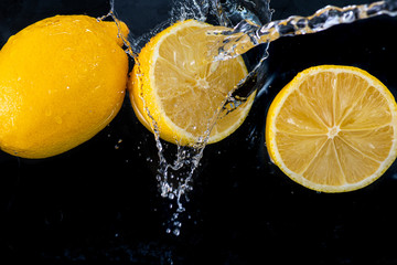 halves of a whole lemon with drops and splashes of water on a black background