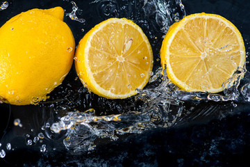 Fototapeta na wymiar halves of a whole lemon with drops and splashes of water on a black background