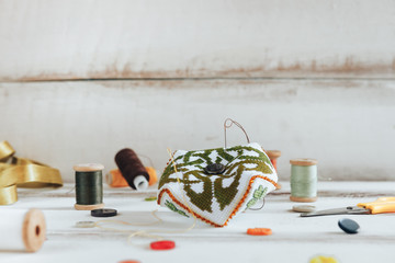 Handmade and needlework. Pin cushion with a simple ornament on a white table. Sewing supplies in the background. Copy space. Side view