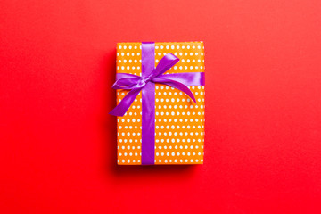 wrapped Christmas or other holiday handmade present in paper with purple ribbon on red background. Present box, decoration of gift on colored table, top view with copy space