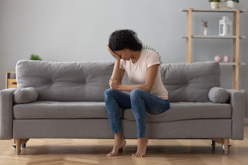 African female crying feels unhappy sitting on couch at home