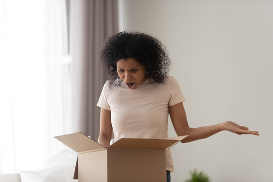 African woman unpacking parcel feels angry see damaged ordered goods