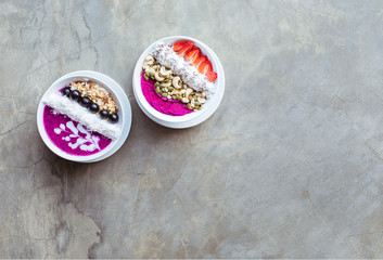 Healthy breakfast smoothie bowls topped with pitaya, cashew, coconut flakes, muesli and strawberry on gray background. Copy space.