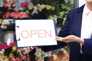 Female business owner holding OPEN sign near flower shop, closeup