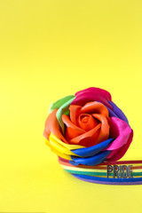 Artificial rose of rainbow color on a yellow background with pride bracelet