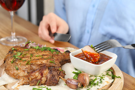 Woman eating delicious grilled pork chop at wooden table, closeup