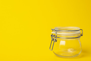 Closed empty glass jar on yellow background, space for text