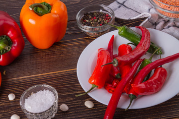 Fresh vegetables and spices on wooden table. Plate with chili peppers, salt, bell peppers and other spices. Culinary background.