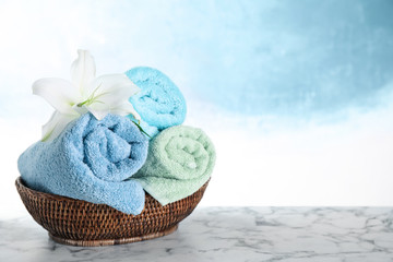 Wicker basket with rolled bath towels and beautiful flower on white marble table. Space for text