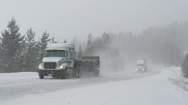 Cars and truck carefully move along a country road during a punishing snowstorm. Freight truck leads the way for other vehicles driving through a blizzard covering rural Canada with fresh snow.