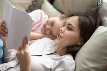 Obraz na płótnie Canvas Loving mother reading book to sleepy cute little daughter