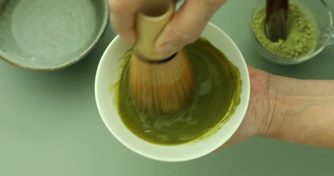 Blending green matcha tea powder in hot water with bamboo whisk to make green matcha tea latte