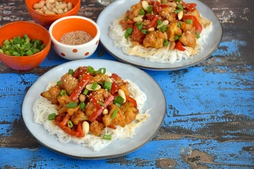 Cauliflower Kung Pao with bell pepper and rice noodles. Garnish with peanuts, scallions and sesame seeds. Vegan food