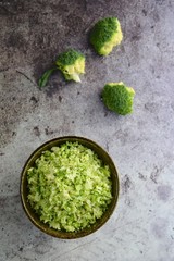 Raw organic broccoli rice in a bowl on grey background
