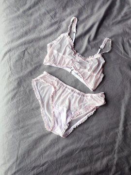 Women's pink gentle sexy lingerie lying at grey bed as background. Vertical photo