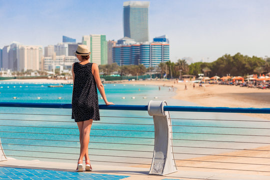 Tourist woman enjoying panoramic view of Abu Dhabi with sea and skyscrapers. Sunny summer day on Abu Dhabi sea shore. Famous tourist destination in UAE. Ideal place for luxury travel and rest