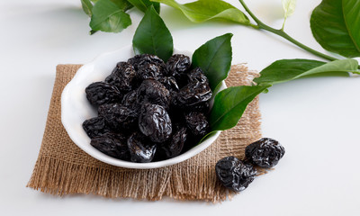 bowl of sweet dried plums with lemon leaves on a white background
