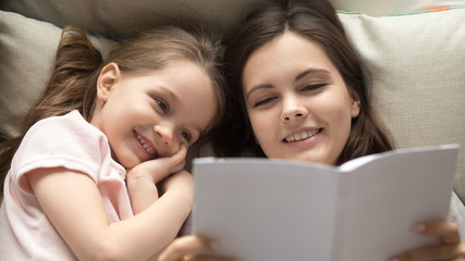 Loving young mother reading book to smiling cute little daughter