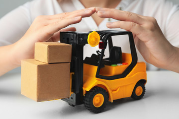 Woman covering toy forklift at white table, closeup. Logistics and wholesale concept