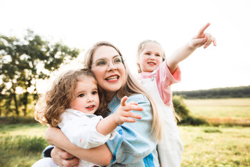 Blonde mother with two cute daughters are walking and having fun outdoors. Stylish, casual clothes.