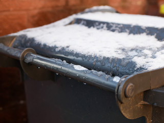Obraz premium Snow on the bin. gray trash can in a row with snow on top on a cold winter day. Snow Thaw. Thaw