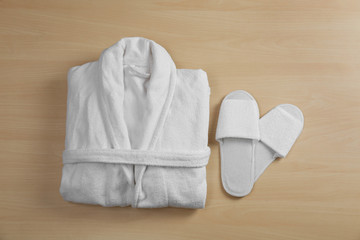 Clean folded bathrobe and slippers on wooden background, flat lay