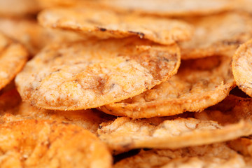 Extreme close up of a pile of organic, crispy, baked, whole grain rice chips with tomato and paprika spices. Gluten free healthy snack. Macro food background, selective focus