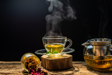 Hot tea in glass teapot and cup with steam on wood table