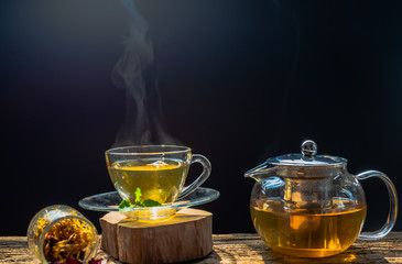 Hot tea in glass teapot and cup with steam on wood table