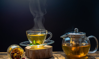 Hot tea in glass cup with steam and lemon .tea leaves and mint herb on wood background