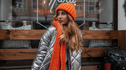Fashionable young woman model in a stylish knitted hat with a vintage warm scarf in a trendy silver...