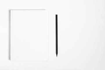Mockup of closed blank square book and black pencil at white textured paper background