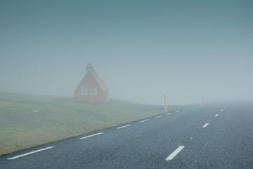 Iceland. The misty landscape of the red Scandinavian House on green grass. Fog
