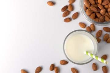Glasses with almond milk and nuts around it on white background, copy space