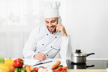 Chef Man Talking On Phone Taking Notes Standing In Kitchen