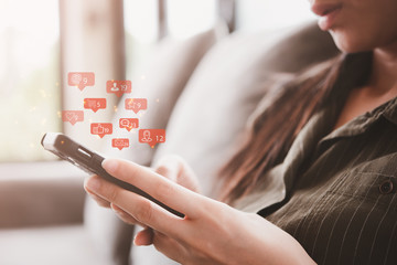 Social media interactions on mobile phone, concept with notification icons of like, message, email, comment and star above smartphone screen, person hands holding device, internet digital marketing