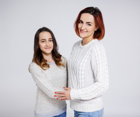 family concept - portrait of smiling mother and daughter posing over grey