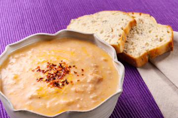 A bowl of creamy soup, with two slices of bread aside to eat with. On a purple table mat.