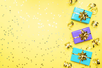 Gift boxes with gold ribbons and bows, confetti stars on a yellow background. Copy space Flat lay. Greeting card for birthday party, Christmas Wedding mother's Day.