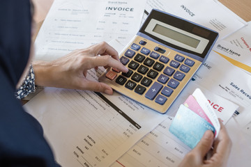 Close up of woman hand using calculator to calculate bills in home office. She also holding credit cards and there are many invoice documents on the table.