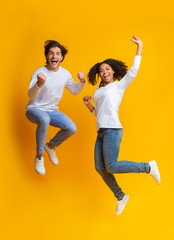 Joyful multiracial couple jumping, having fun together on yellow background