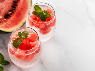 Watermelon ice with sparkling water or soda in glass tumbler. Summer party idea and recipe, add color and flavor for soda or other drink. Copy space. White marble background