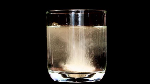 Tablet dissolve in rotating glass with water, on black background. Preparation of instant drink from soluble tablet, shorter version.
