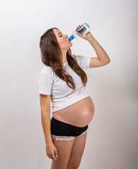 beautiful pregnant brunette woman drinking water from the bottle on isolated white background