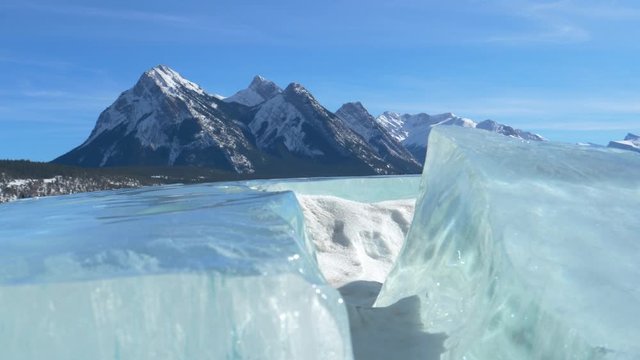 CLOSE UP: Snow gathers and gimmers in the deep cracks in frozen Lake Abraham on a sunny winter day. Spectacular glacial ridge towers over the Jasper National Park. Stunning crystal clear glacial lake.