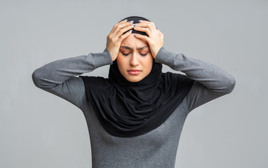 Depressed muslim woman in hijab holding head in hands