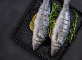 fresh sea bass with lemon and rosemary on a black baking sheet, preparation for baking